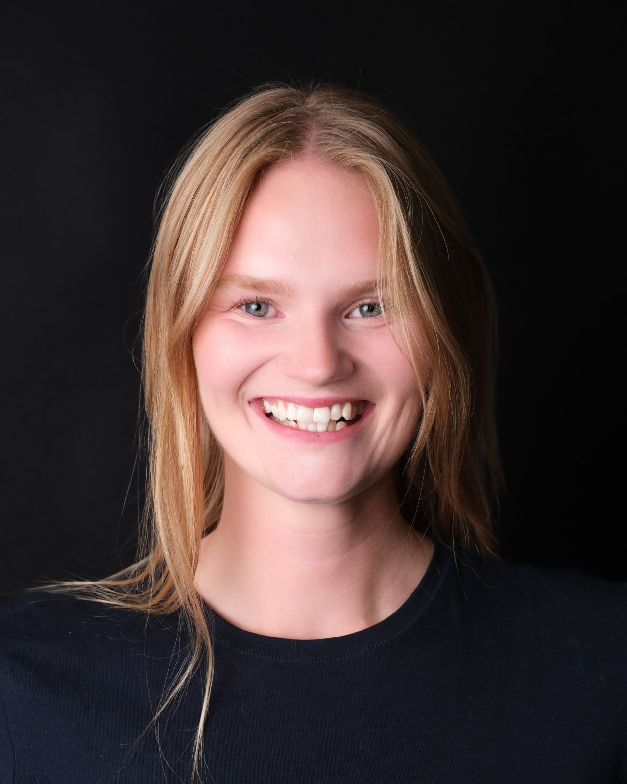 Rebecka Norling leende i mörk tröja mot svart bakgrund